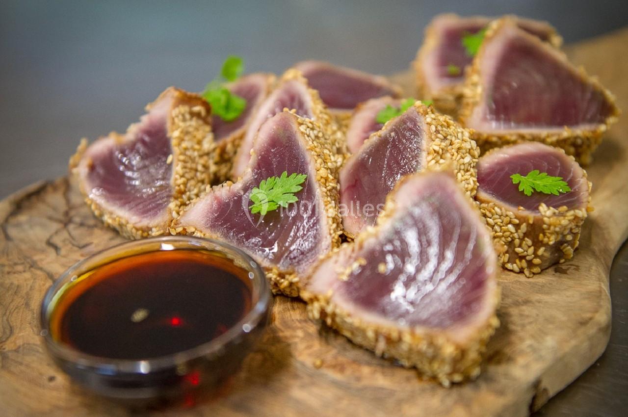 Tranches de thon mi-cuit en croûte de sésame servies sur une planche en bois avec une sauce dans un bol.
