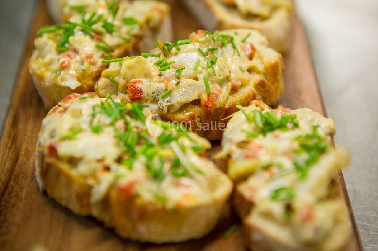 Tranches de pain garnies de fromage fondu, légumes et ciboulette, servies sur une planche en bois.