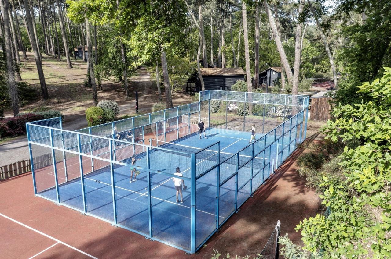 Terrain de padel extérieur entouré de grillages, situé dans un cadre boisé avec plusieurs joueurs en action.