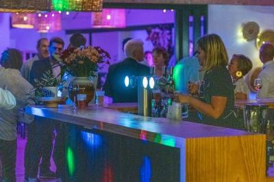 Bar animé avec des lumières colorées, des clients discutant et des paniers suspendus en décoration.