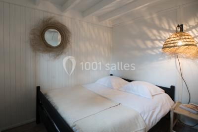 Cabane en bois sombre entourée de grands pins dans une forêt, avec lumière du soleil filtrant à travers les arbres.