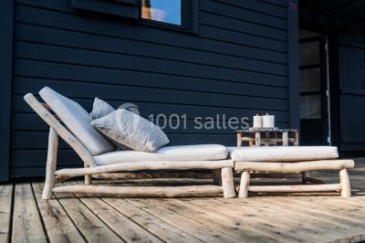 Cabane en bois sombre entourée de grands pins dans une forêt, avec lumière du soleil filtrant à travers les arbres.