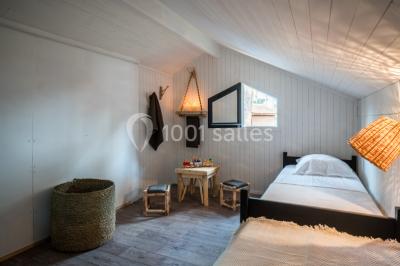Cabane en bois sombre entourée de grands pins dans une forêt, avec lumière du soleil filtrant à travers les arbres.
