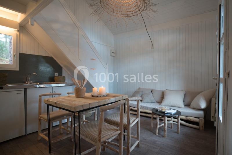 Intérieur d'une petite pièce lumineuse avec coin cuisine, table en bois, canapé beige et décoration minimaliste.