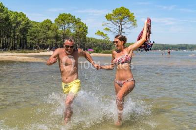 Cabane en bois sombre entourée de grands pins dans une forêt, avec lumière du soleil filtrant à travers les arbres.