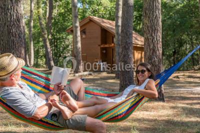 Cabane en bois sombre entourée de grands pins dans une forêt, avec lumière du soleil filtrant à travers les arbres.