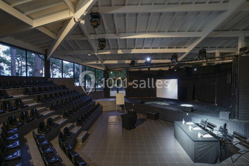 Salle de conférence moderne avec gradins, scène équipée d'un écran de projection et éclairage professionnel.