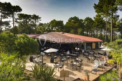 Cabane en bois sombre entourée de grands pins dans une forêt, avec lumière du soleil filtrant à travers les arbres.