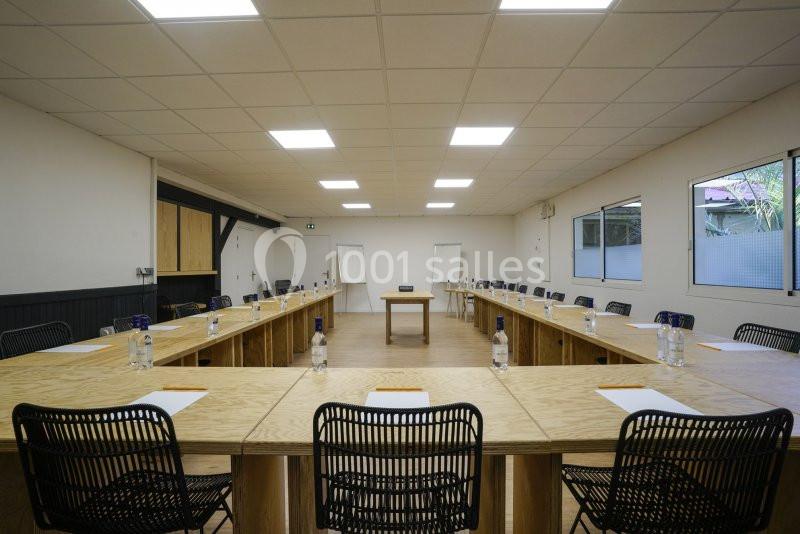 Salle de réunion lumineuse avec tables disposées en U, chaises noires, bouteilles d'eau et blocs-notes.