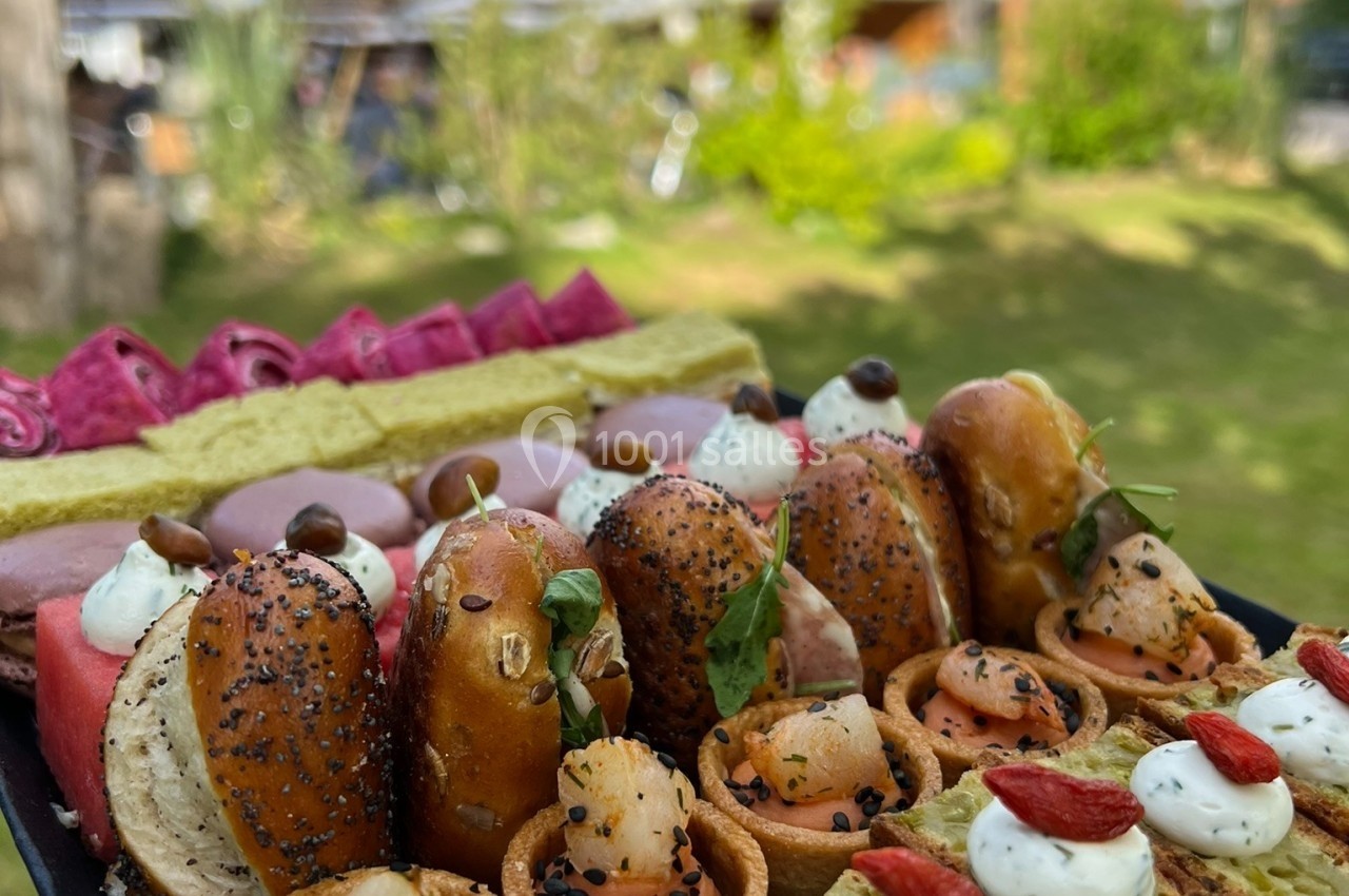 Plateau de bouchées variées comprenant bagels, toasts et amuse-bouches, présenté en extérieur dans un jardin verdoyant.