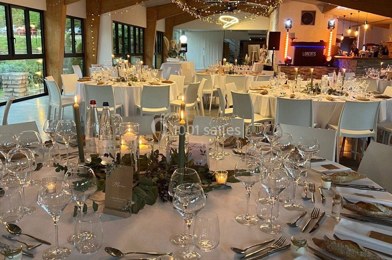 Salle de réception décorée avec des tables rondes dressées, bougies, guirlandes lumineuses et ambiance festive.
