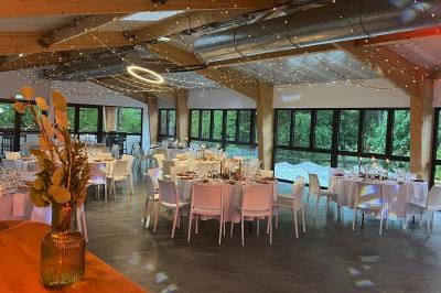 Salle de réception décorée avec des tables rondes, nappes blanches, serviettes orange et chaises blanches.