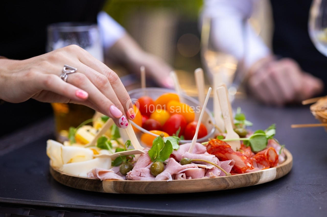 Plateau de charcuterie et fromages avec tomates cerises, olives et herbes, une main prenant un morceau.