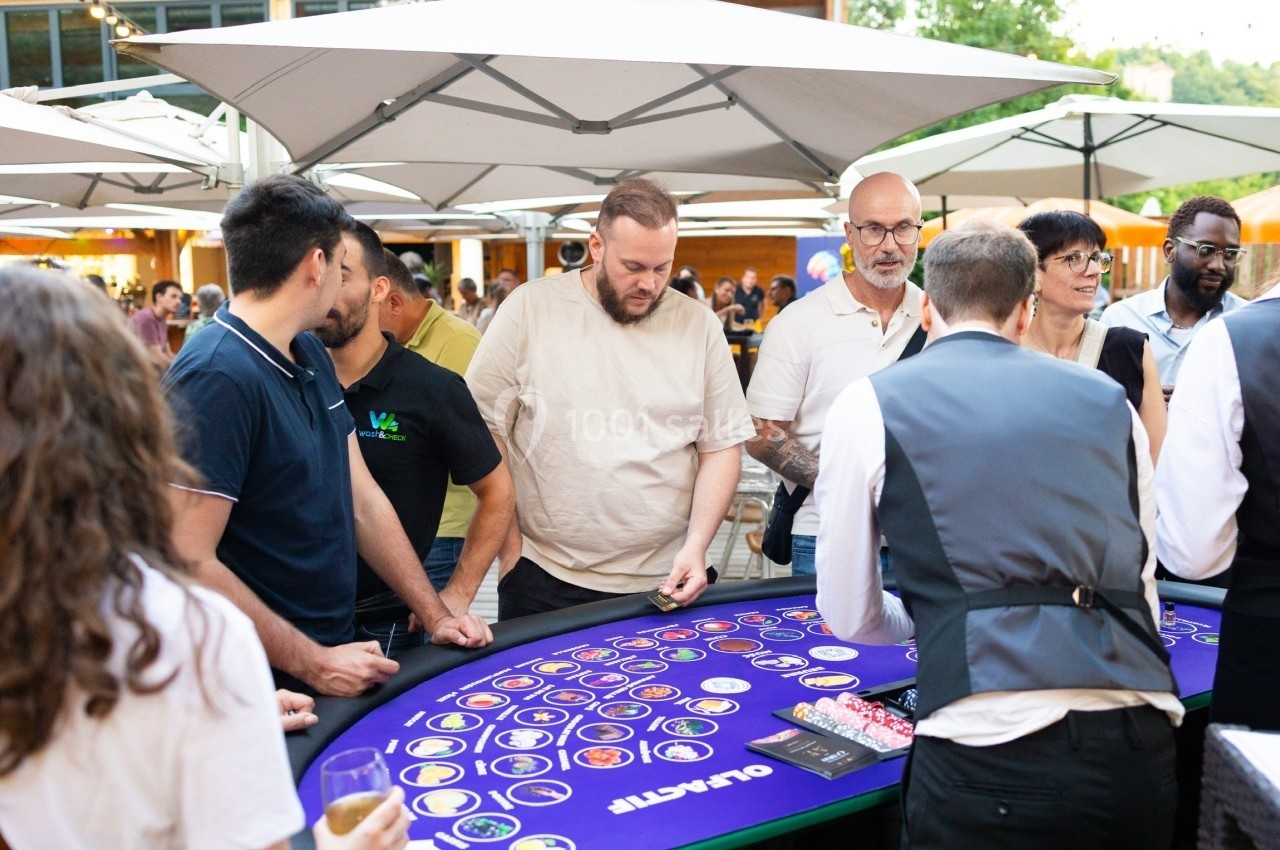 Des personnes jouent autour d'une table de casino en plein air, sous des parasols.