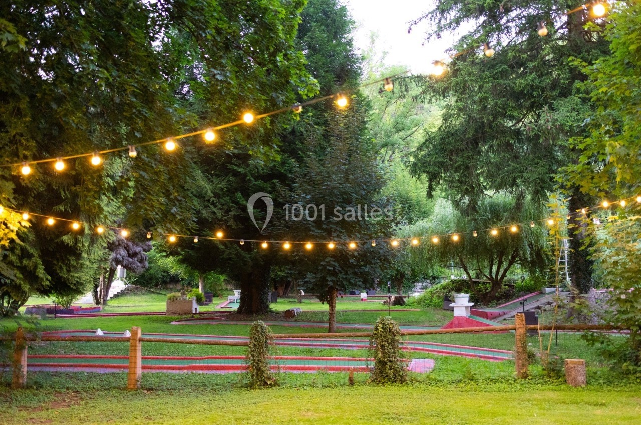 Terrain de mini-golf en extérieur entouré d'arbres, éclairé par des guirlandes lumineuses suspendues.