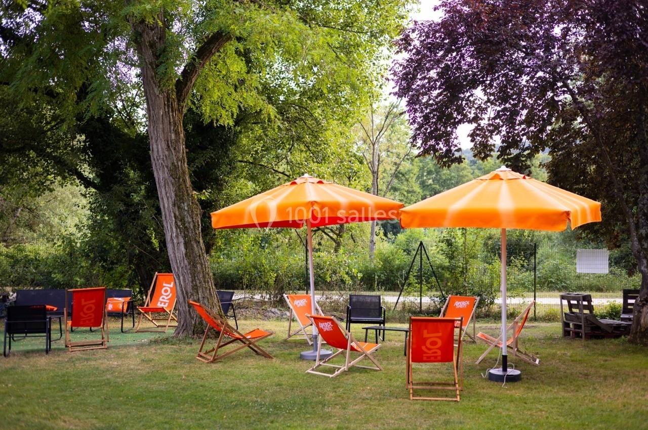 Chaises longues et parasols orange disposés sur une pelouse ombragée, entourée d'arbres et de verdure.