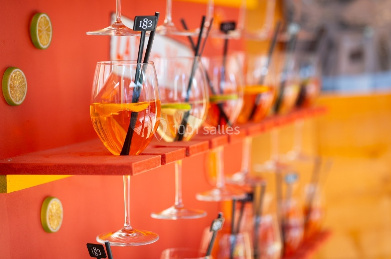 Verres de cocktail garnis de tranches d'agrumes alignés sur des étagères rouges dans un décor coloré.