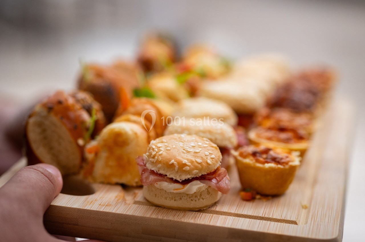 Plateau en bois garni de divers amuse-bouches, incluant mini-burgers, roulés et bouchées salées.