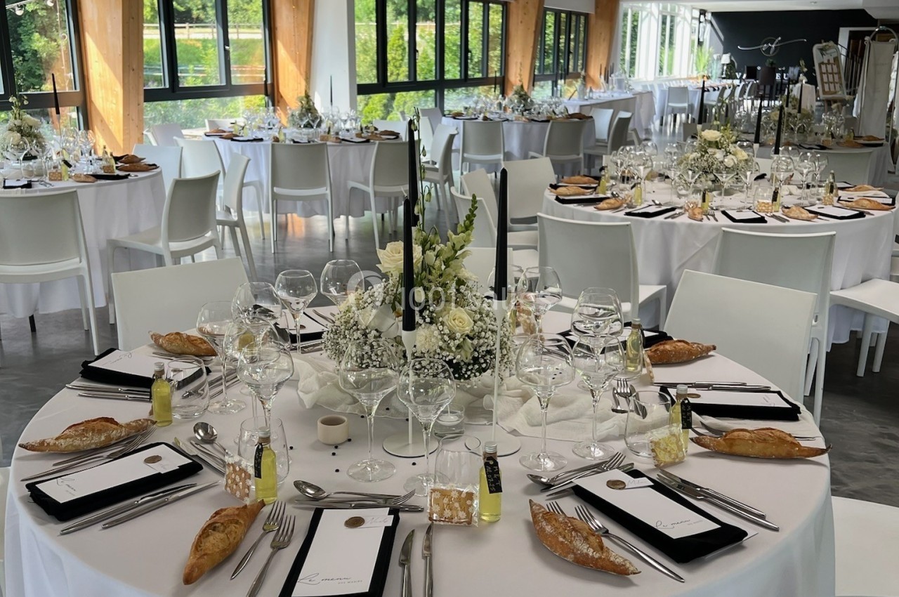 Salle de réception lumineuse avec tables rondes dressées, décorations florales blanches et couverts élégants.
