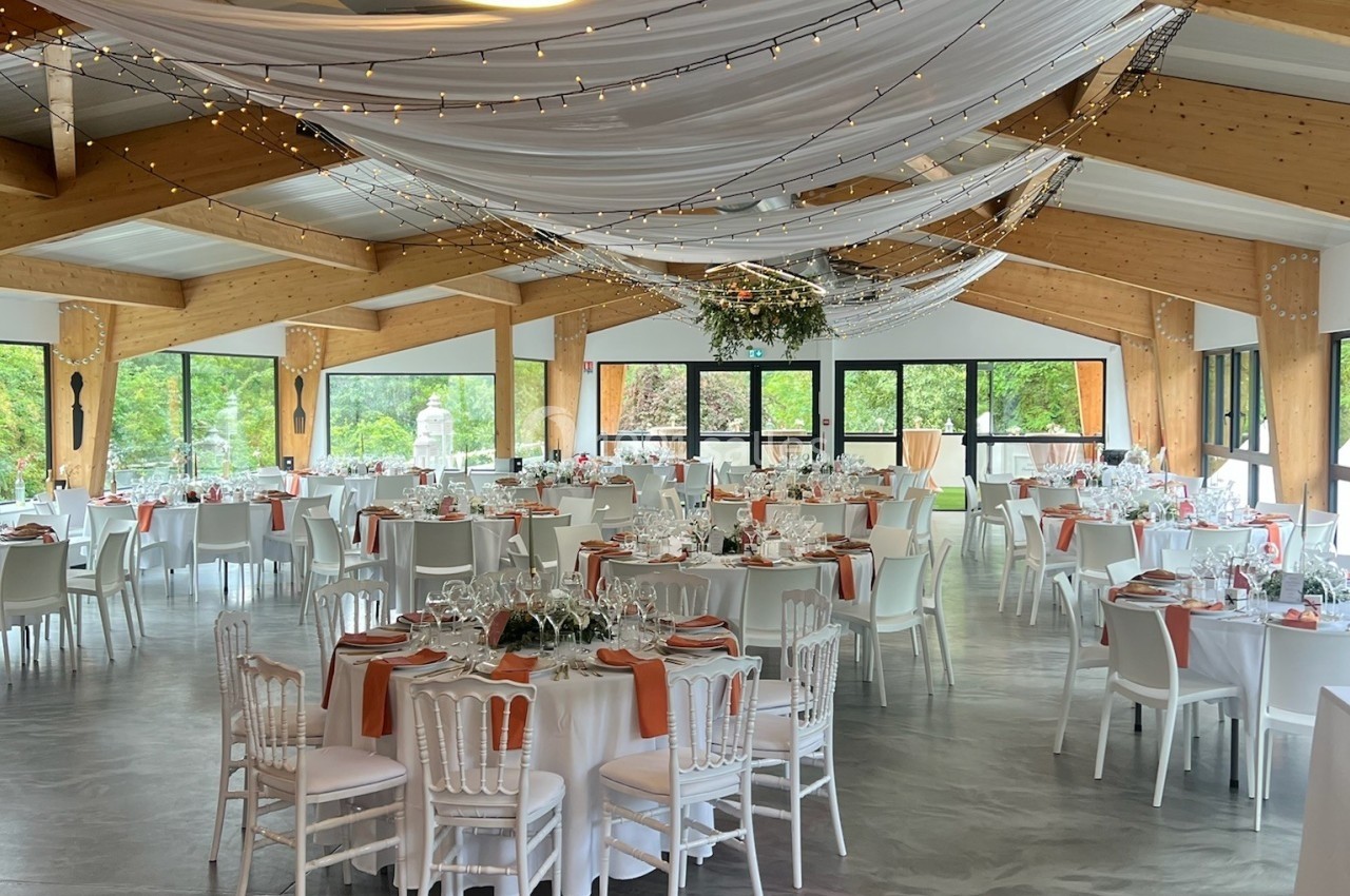 Salle de réception décorée avec des tables dressées, des nappes blanches et des guirlandes lumineuses suspendues.