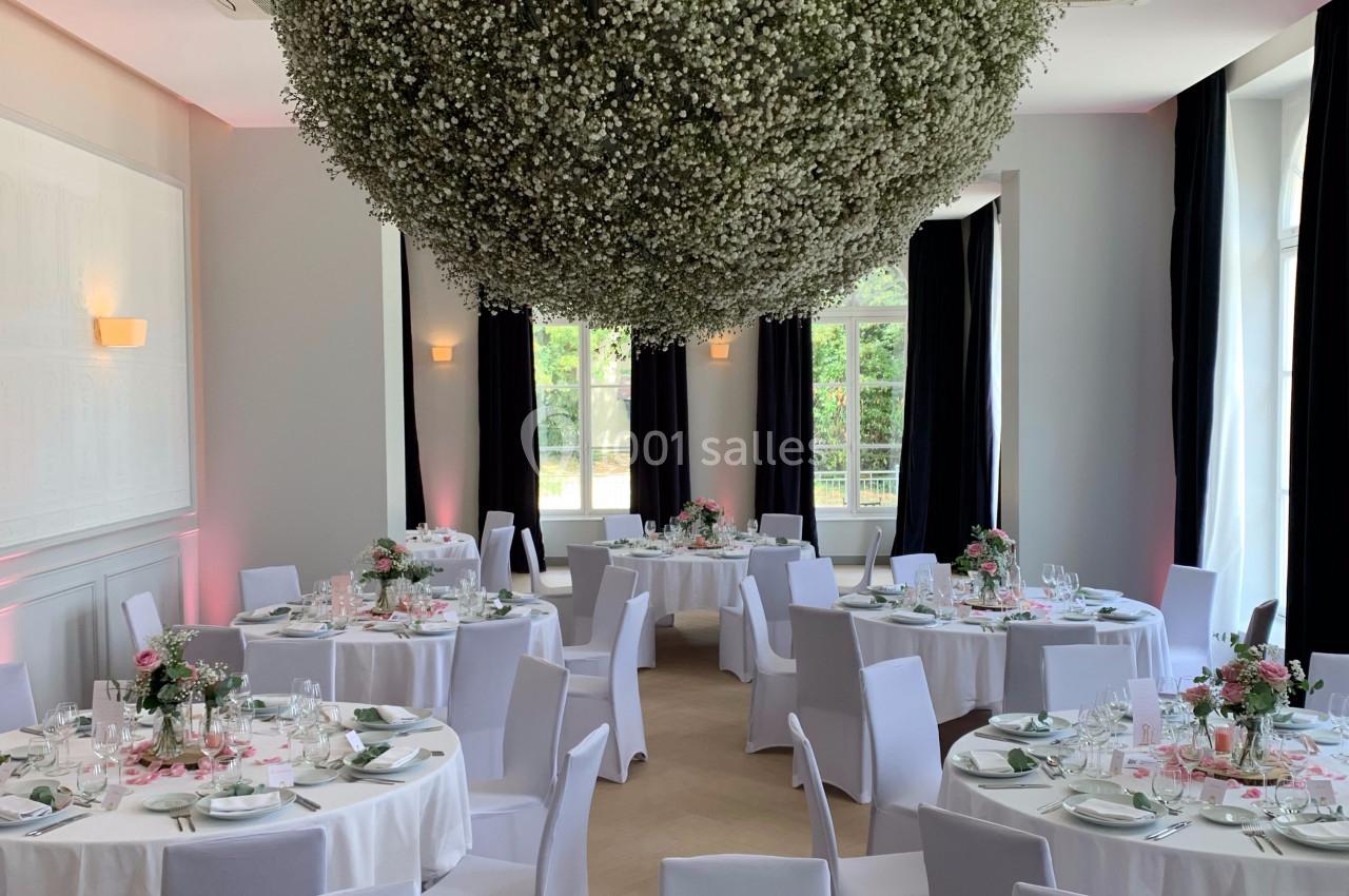 Salle de réception élégante avec tables décorées de fleurs roses et blanches, et une grande suspension florale.