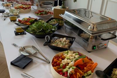 Buffet de petit-déjeuner avec viennoiseries, pain, confiture et grille-pain, devant une fenêtre et des fleurs décoratives.