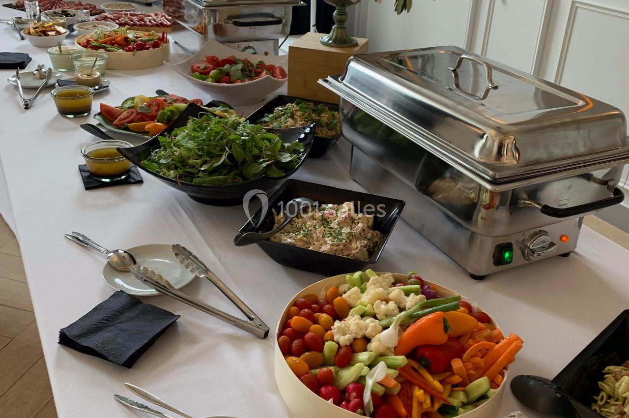 Buffet varié avec plats chauds en chafing dishes, salades, légumes frais, fromages et décoration florale.
