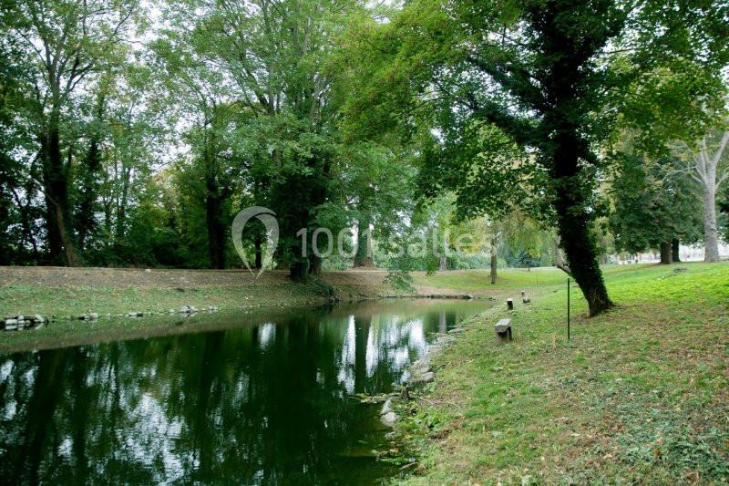 Étang entouré d'arbres et de pelouse, avec des bancs en bois disposés le long de la rive.