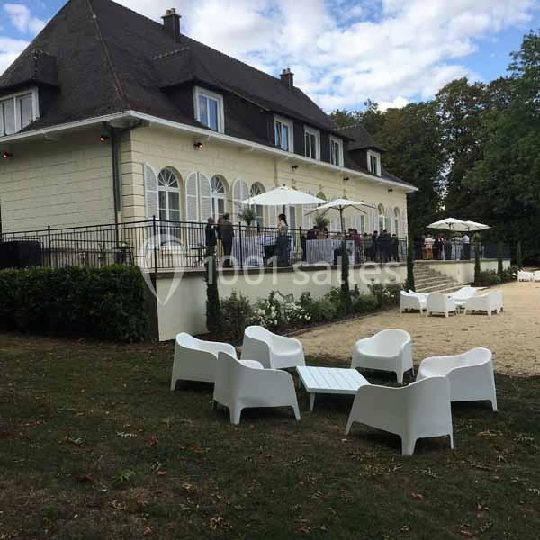 Façade d'un bâtiment élégant avec terrasse animée, mobilier de jardin blanc sur pelouse au premier plan.