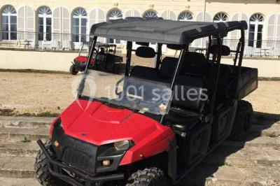 Véhicule tout-terrain rouge stationné sur des marches en pierre devant un bâtiment avec de grandes fenêtres.
