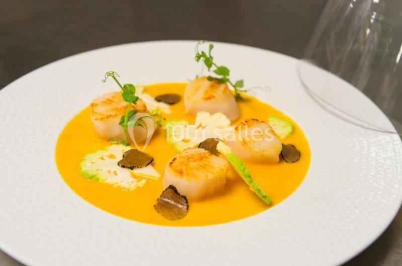 Assiette de noix de Saint-Jacques poêlées servies sur une crème orange avec truffes, chou-fleur et herbes fraîches.