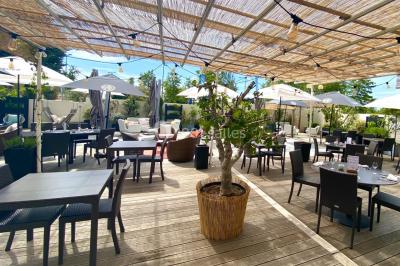 Salle de restaurant lumineuse avec des tables en bois, chaises bleues et grandes fenêtres laissant entrer la lumière…