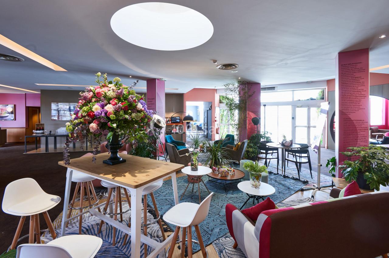 Espace intérieur lumineux avec mobilier moderne, plantes décoratives et grand bouquet de fleurs sur une table haute.