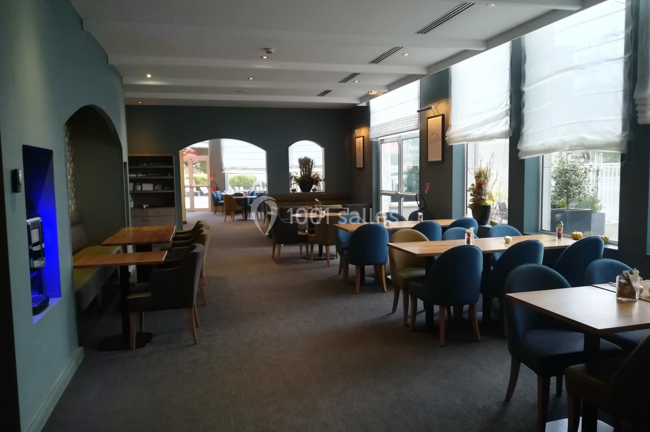 Salle de restaurant lumineuse avec des tables en bois, chaises bleues et grandes fenêtres laissant entrer la lumière…