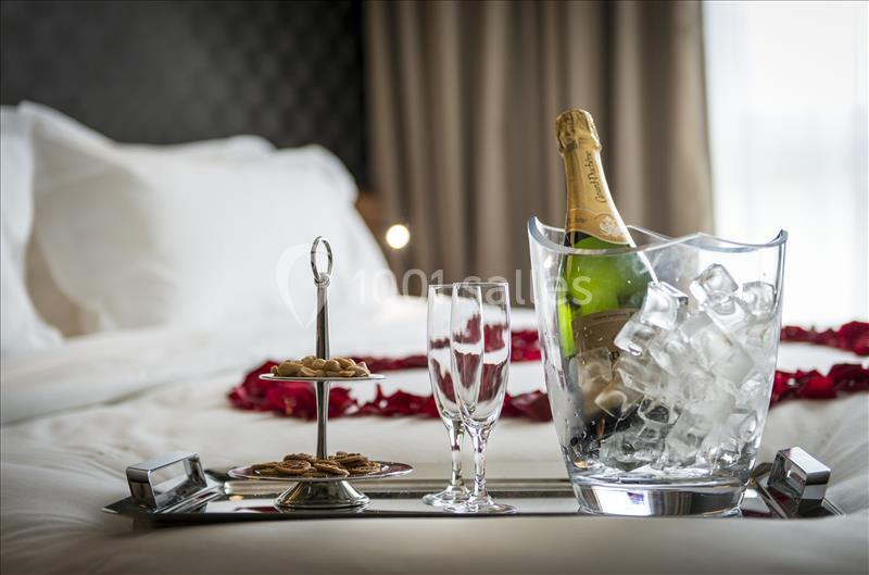 Seau à glace avec bouteille de champagne, flûtes et plateau de biscuits sur un lit décoré de pétales rouges.