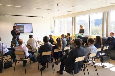 Façade vitrée d'un bâtiment moderne avec une terrasse en bois éclairée par le soleil.