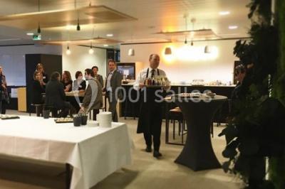 Façade vitrée d'un bâtiment moderne avec une terrasse en bois éclairée par le soleil.