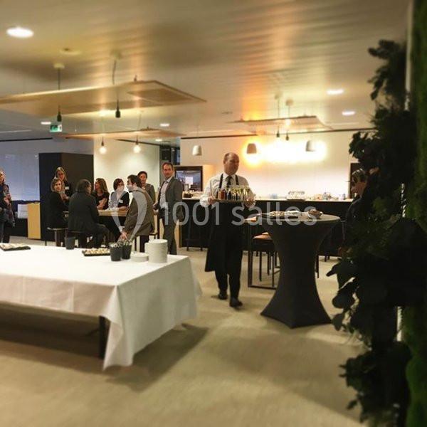 Un serveur portant un plateau de boissons dans une salle de réception avec des invités debout en arrière-plan.