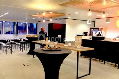 Façade vitrée d'un bâtiment moderne avec une terrasse en bois éclairée par le soleil.