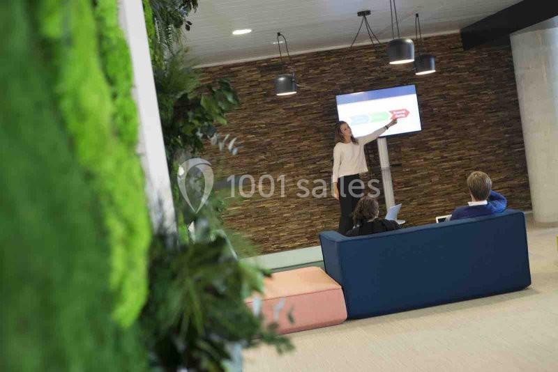 Une femme présente un graphique sur un écran dans un espace de travail moderne avec des plantes et des sièges.