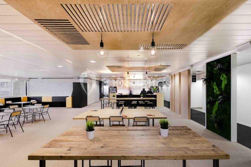 Espace de travail moderne avec tables en bois, plantes décoratives, éclairage suspendu et coin restauration.