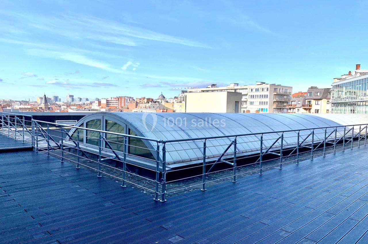 Toit-terrasse avec garde-corps, surface en bois et structure vitrée arrondie, vue sur des bâtiments urbains.