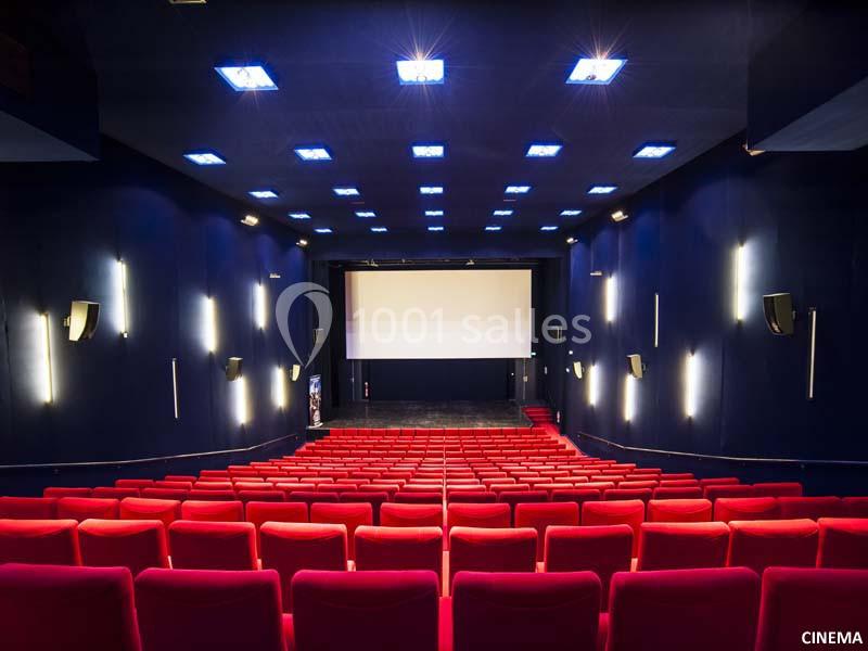 Salle de cinéma vide avec rangées de fauteuils rouges, écran blanc et éclairage au plafond.