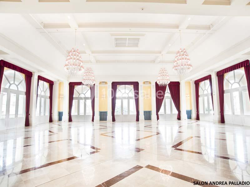 Salle spacieuse et lumineuse avec sol en marbre, grandes fenêtres cintrées, rideaux rouges et lustres imposants.