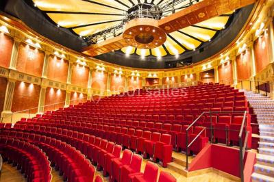 Salle de conférence lumineuse avec des rangées de chaises blanches et une table en bois au premier plan.