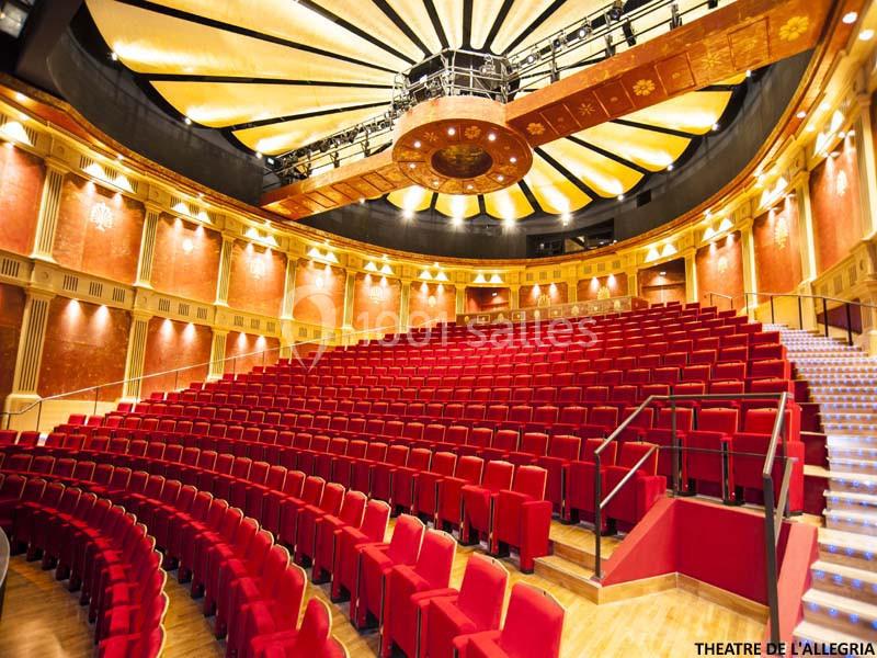 Salle de théâtre avec sièges rouges, balcons en bois et plafond décoratif circulaire éclairé.