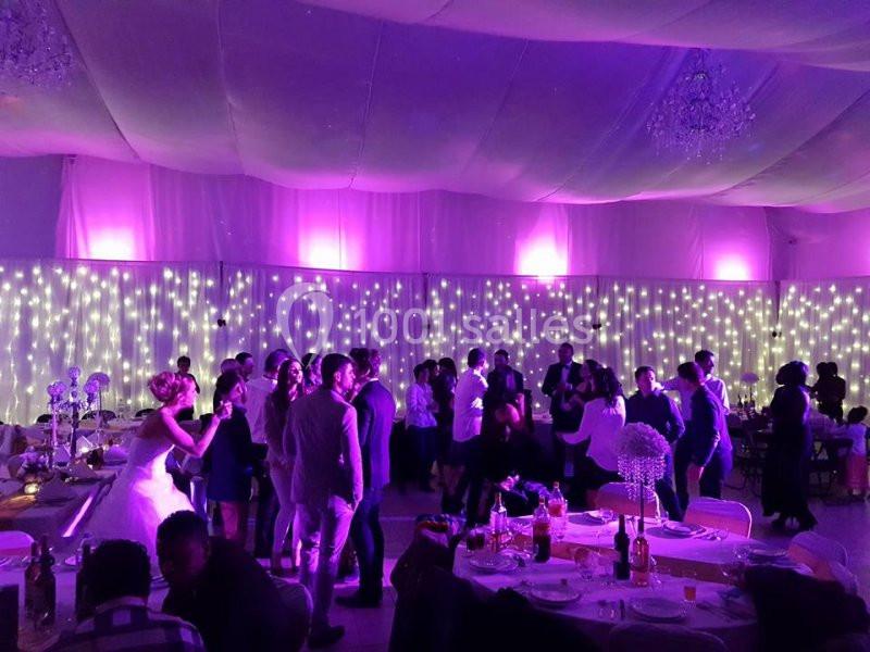 Salle de réception décorée de guirlandes lumineuses violettes, avec des invités dansant et discutant.