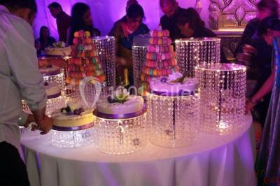 Salle de réception décorée avec des lumières violettes, une arche florale et des chaises transparentes disposées autour de…