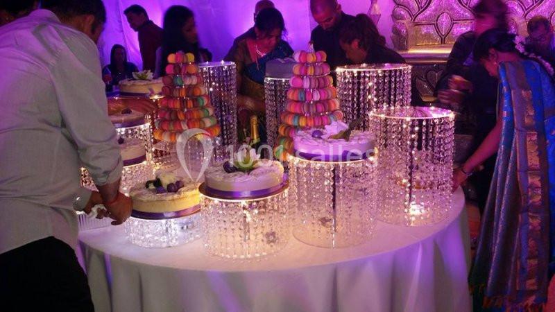 Table ornée de gâteaux et de macarons colorés sur des présentoirs éclairés, entourée de convives.