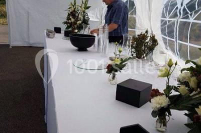 Salle de réception décorée avec des lumières violettes, une arche florale et des chaises transparentes disposées autour de…